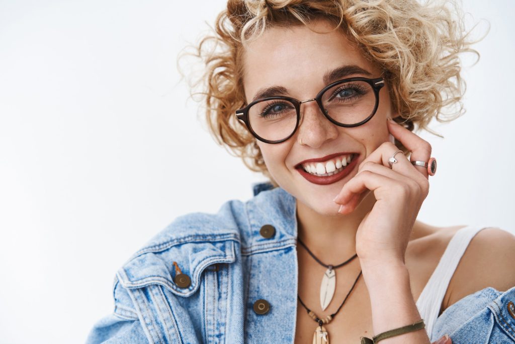 Une charmante amie séduisante et sensuelle avec une coiffure courte et bouclée dans des lunettes, un rouge à lèvres et une veste en jean